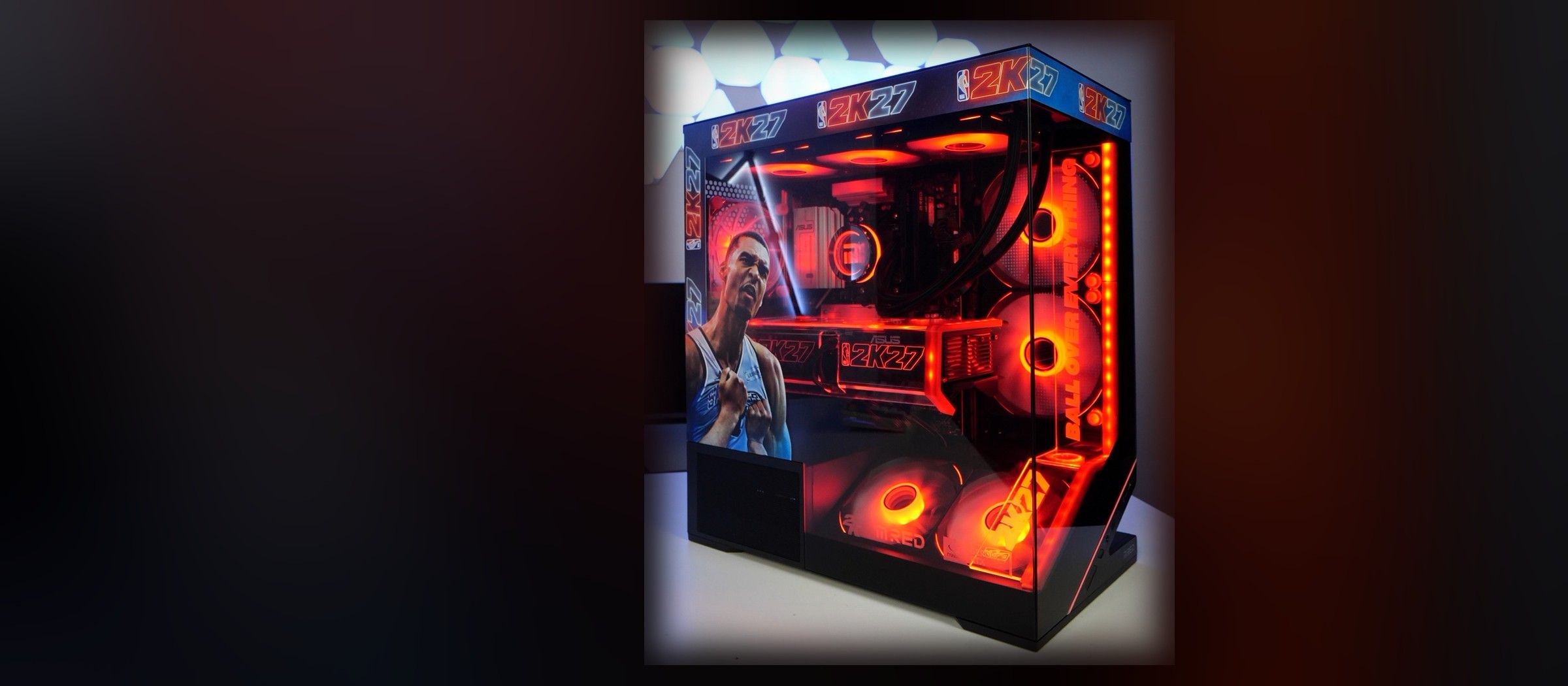 Le boîtier aux couleurs de NBA 2K27, vu de trois quarts : bande de logos sur le dessus, joueur imprimé sur le panneau de gauche, ventilateurs éclairés en rouge derrière le verre