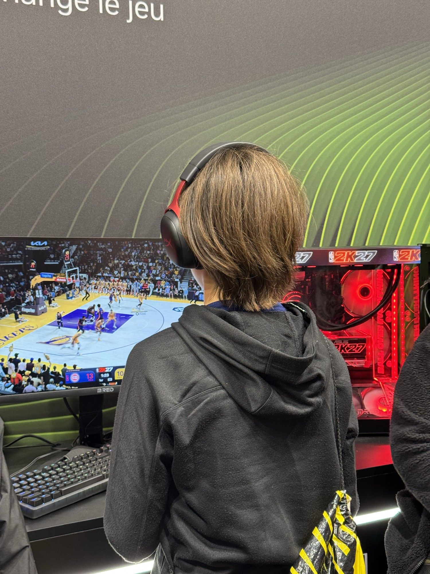 Une partie de NBA 2K27 en cours sur l’écran M.RED de la station, le boîtier aux couleurs du jeu posé à droite